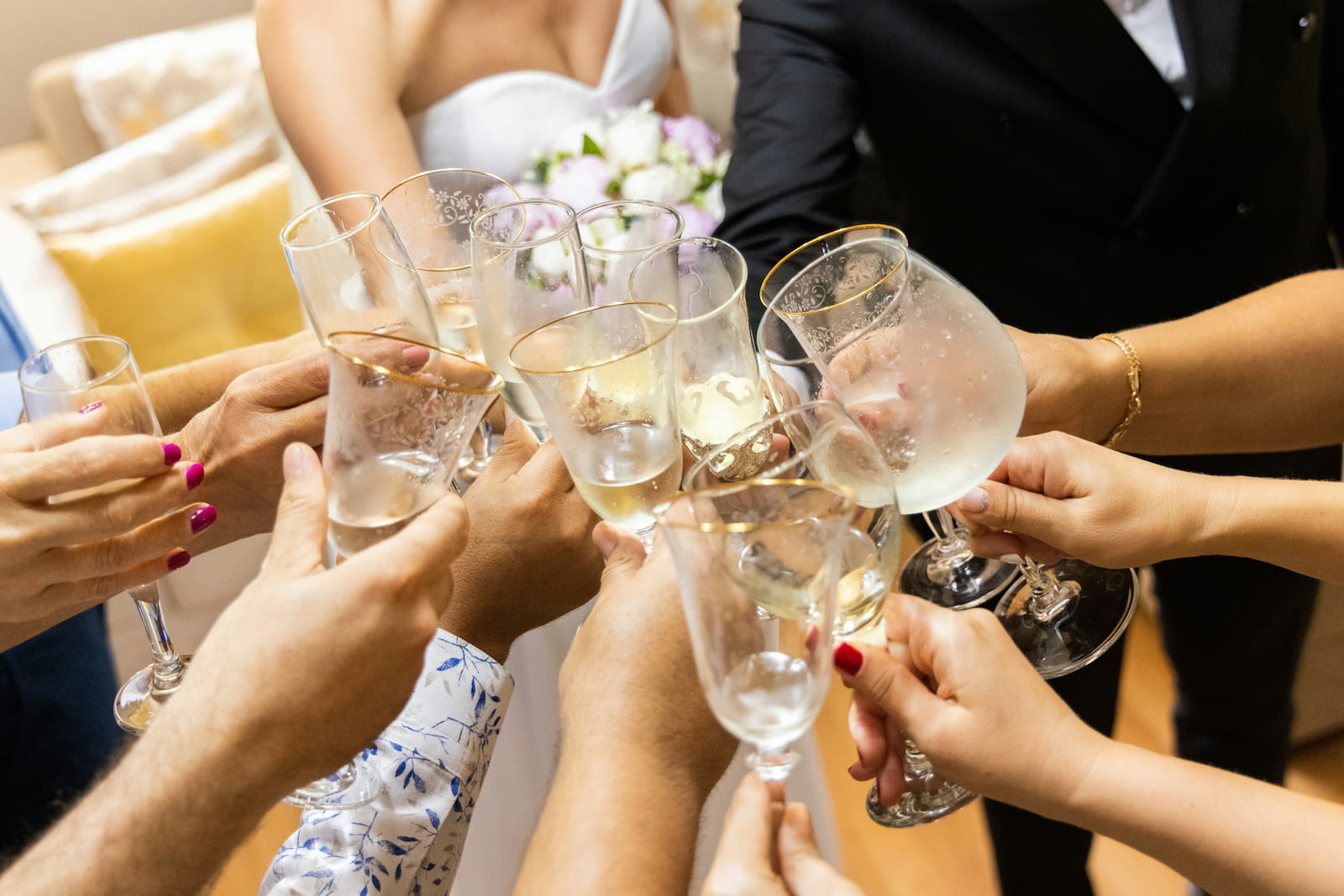 Wedding guests raising gold-rimmed champagne glasses in a toast, bride and groom behind