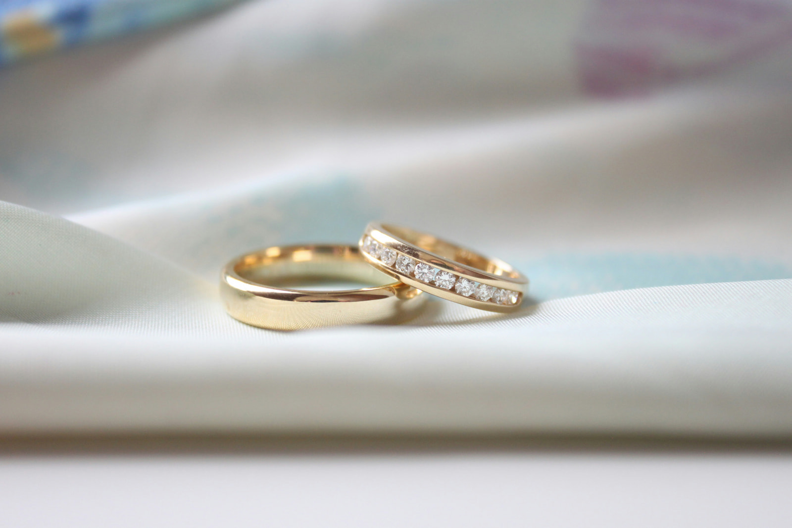Two gold wedding rings, one set with diamonds, resting on soft pale fabric